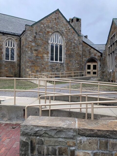 A wheelchair ramp with handrails in front of the side entrance to the church, providing accessible entrance for people with mobility impairments