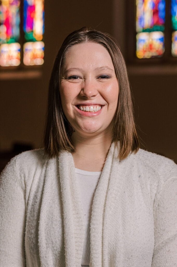 A portrait of Rachel Donnell, nursery care leader, standing in front of the stained glass windows in the sanctuary