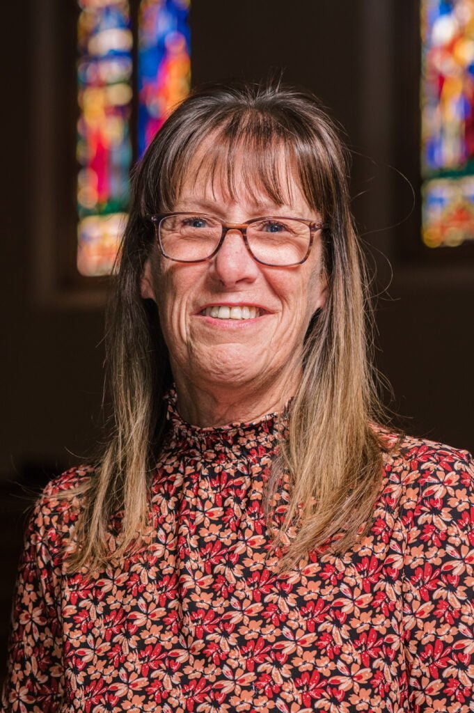 A portrait of Wendy Donnell, director of Christian education, standing in front of the stained glass windows in the sanctuary