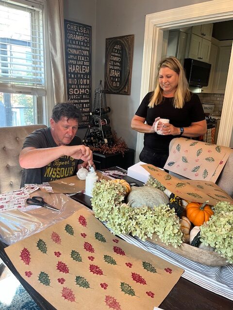 Man making Christmas tree ornament while smiling woman observes