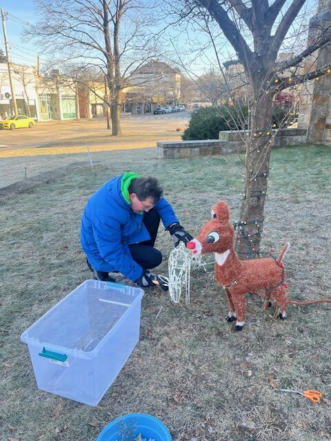 man in blue parka putting in stakes to secure a lighted deer.