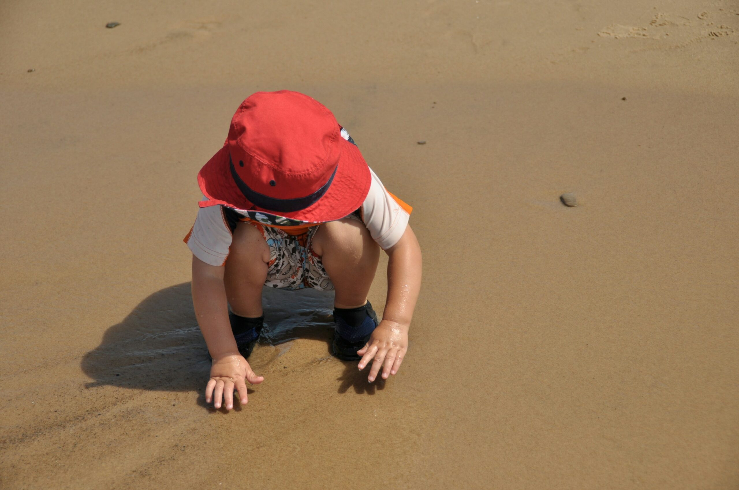 child in red hat touching sand