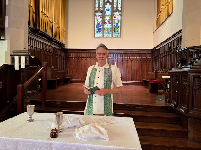 The Reverend Rick Chrisman, minister, in front of sanctuary, standing at communion table
