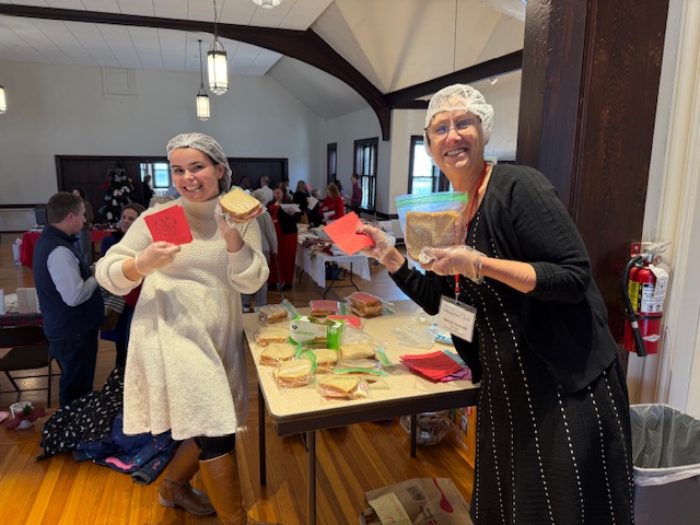 Two women with hairnets holding notecards and smiling