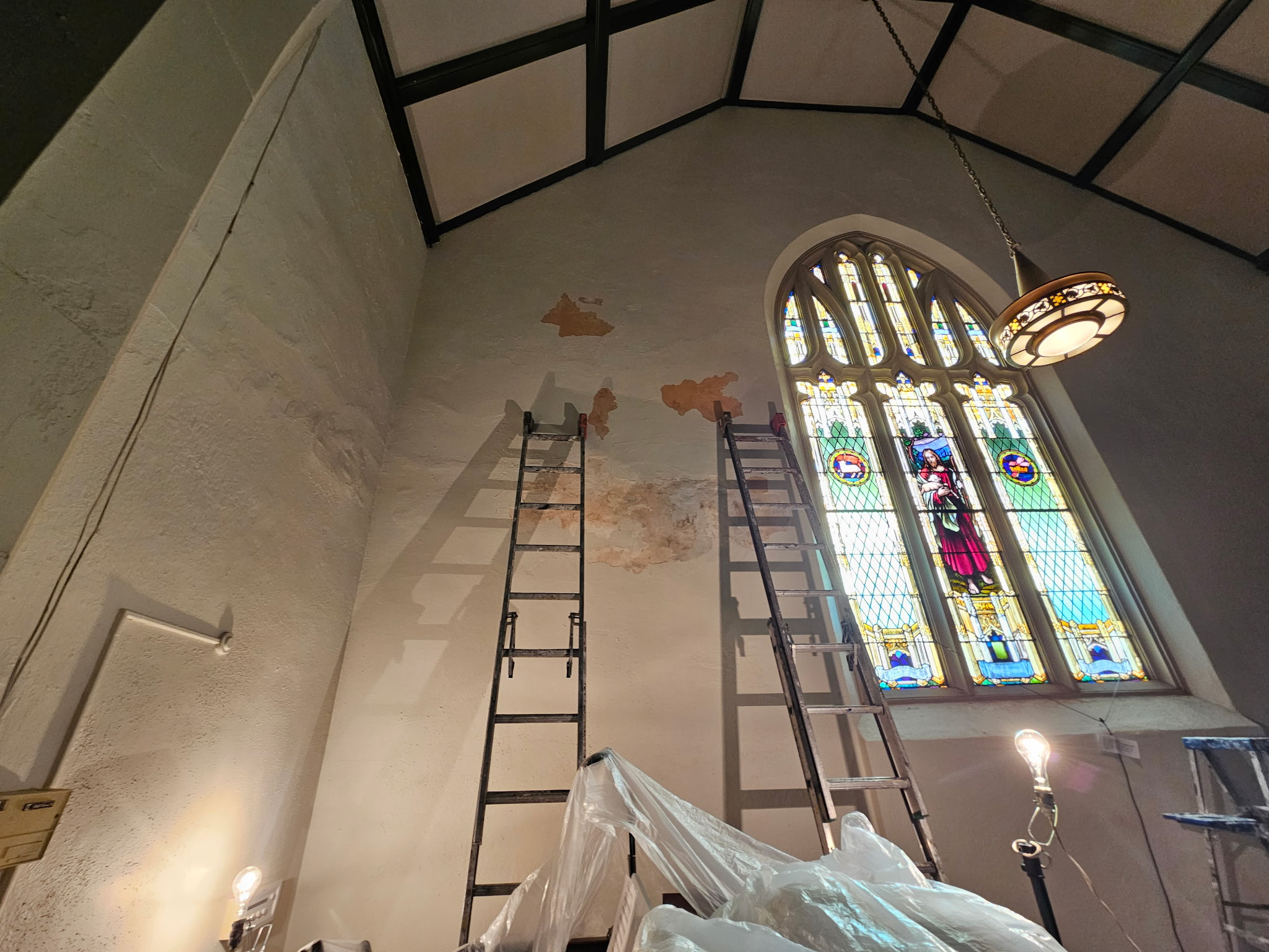 Damaged wall with two ladders alongside stained glass window